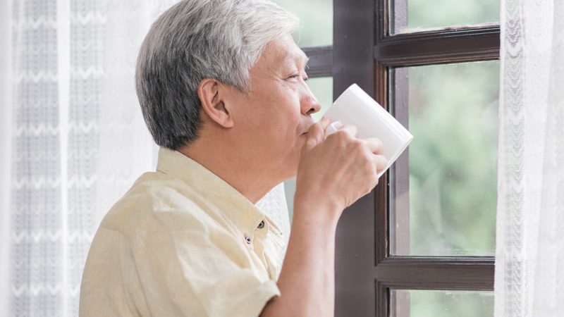 happy-asian-elderly-man-drinking-cup-coffee-tea-near-window